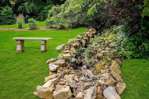 Un jardín con muro de piedra, una estatua y un banco.