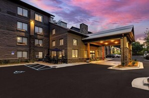 A multi-story hotel with a covered outdoor seating area and a parking lot. - Graystone Lodge, an Ascend Collection Hotel (Boone)