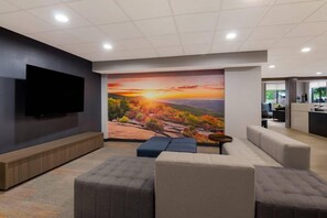 En modern inredning med en stor platt-TV som är monterad på väggen, en sittgrupp med soffor och ett soffbord samt en väggmålning som föreställer ett solnedgångslandskap.