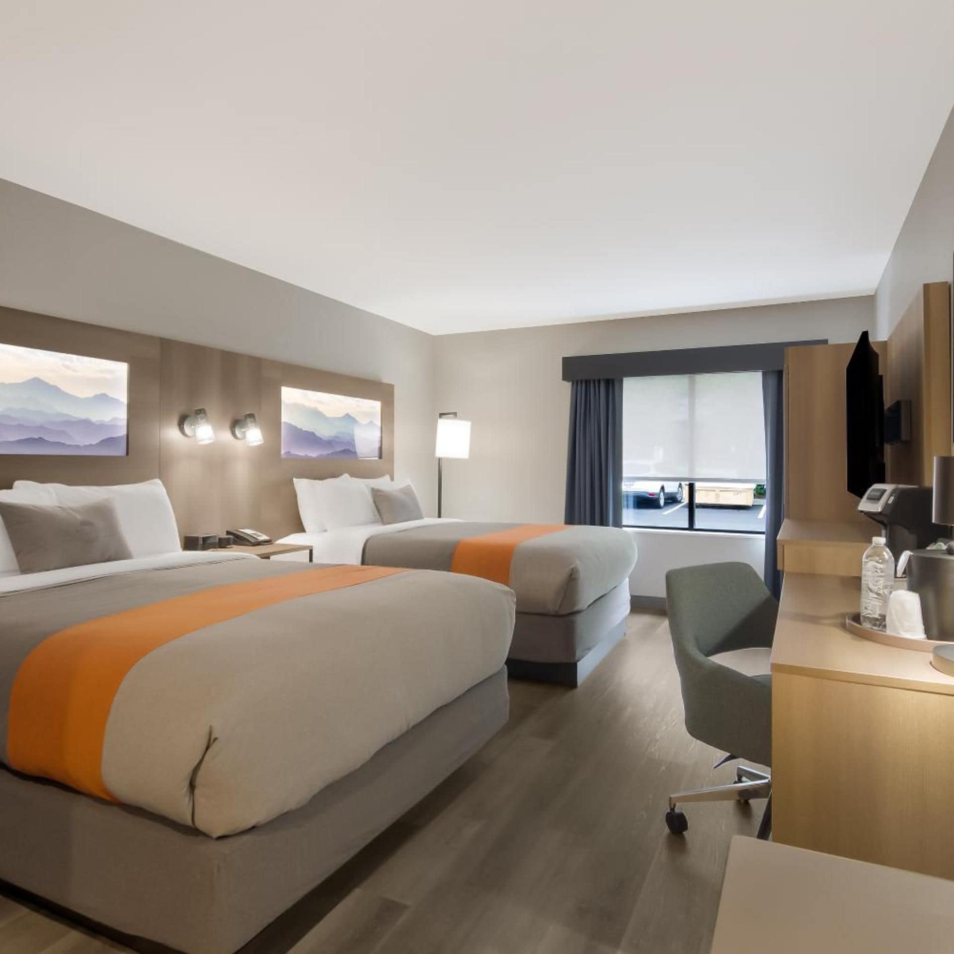 A hotel room with two beds, a desk, a chair, and a window with a view.