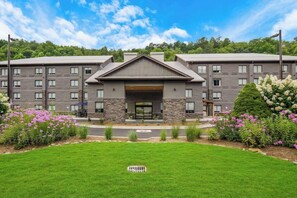 A multi-story hotel with a central entrance, surrounded by a well-maintained lawn and flowering plants. - Graystone Lodge, an Ascend Collection Hotel (Boone)