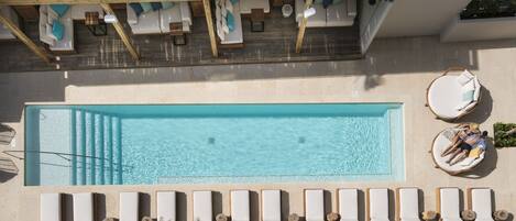 Una piscina rectangular con sillones de jardín y tumbonas alrededor.