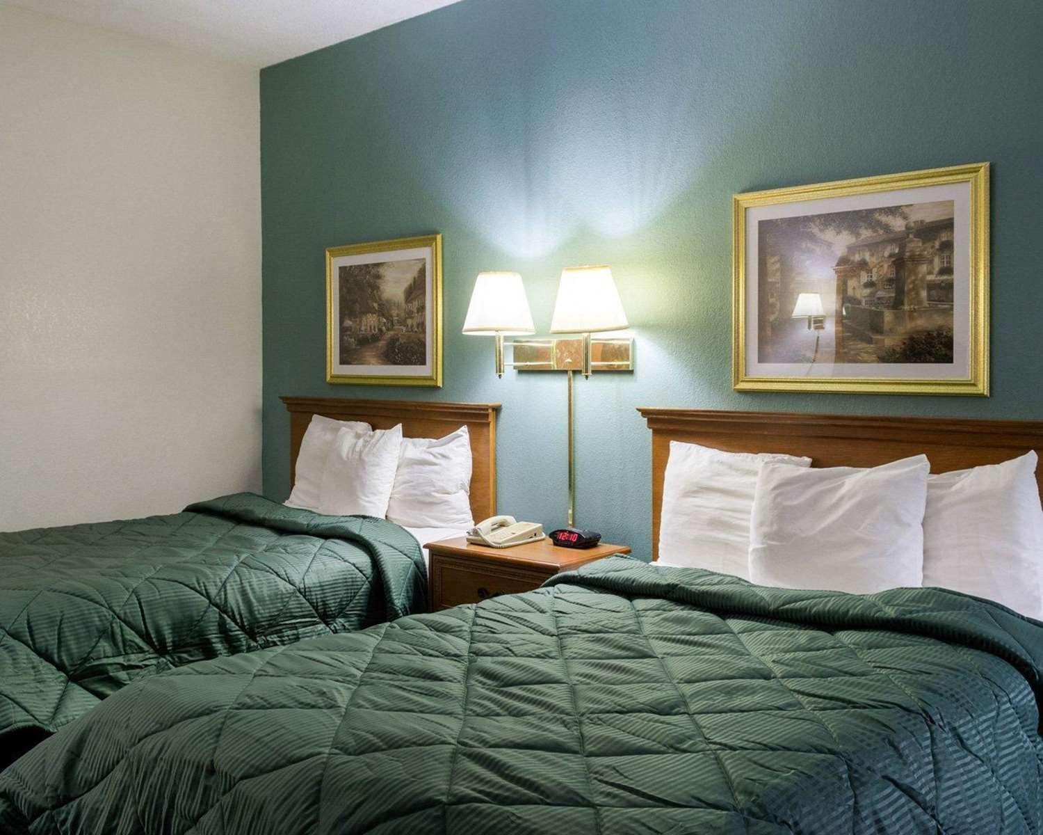 A hotel room with two beds, a nightstand with a lamp, and two framed pictures on the wall.