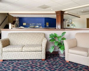 A reception area with a blue wall, a reception desk, a patterned sofa, a potted plant, and a carpeted floor.