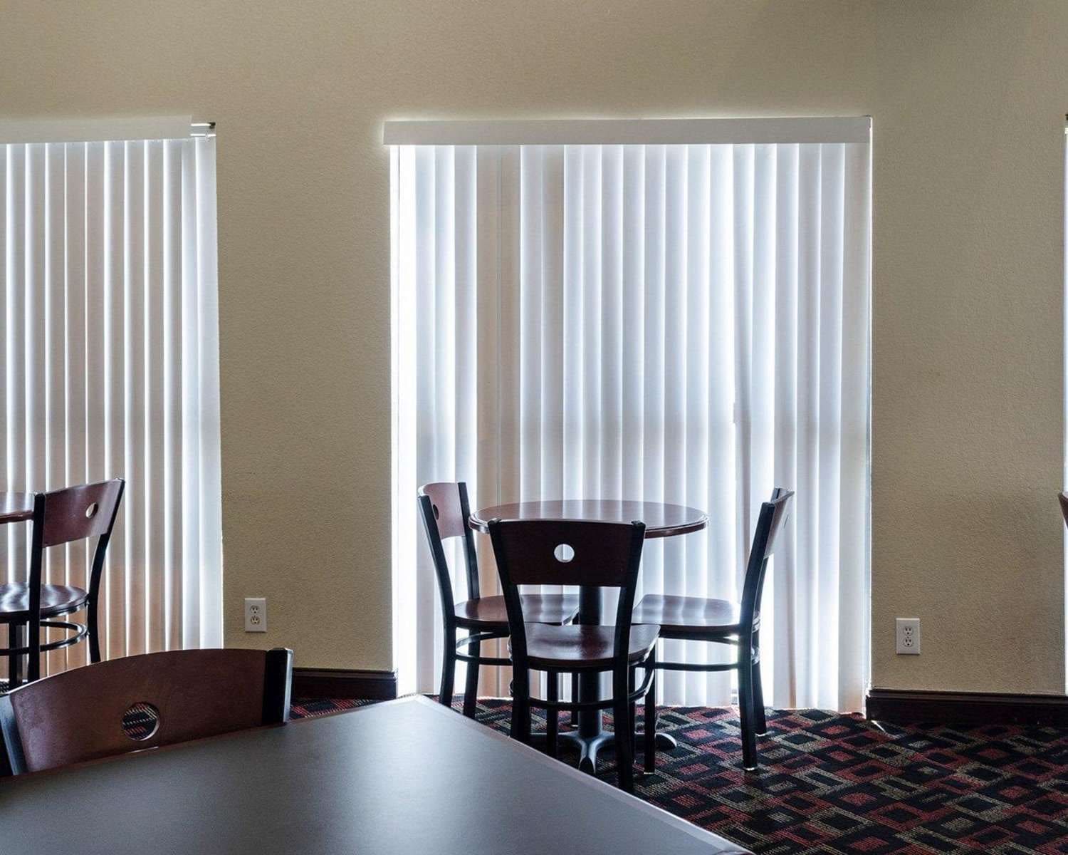 A room with a dining table and chairs, a window with blinds, and a carpeted floor.
