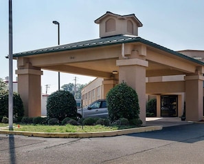 A building with a covered entrance, columns, and a car parked in front.
