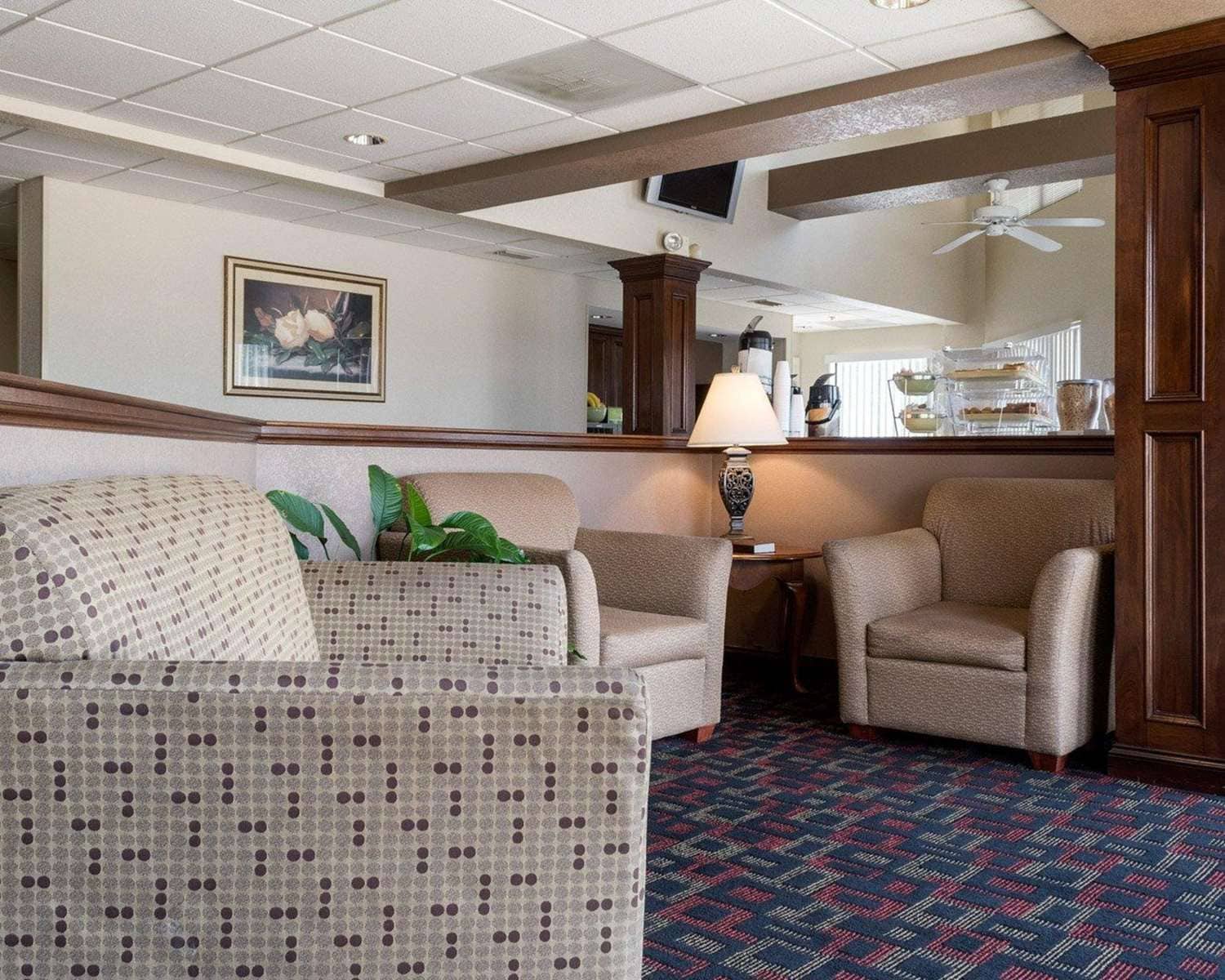 A hotel room with a patterned sofa, two armchairs, a coffee station, and a ceiling fan.