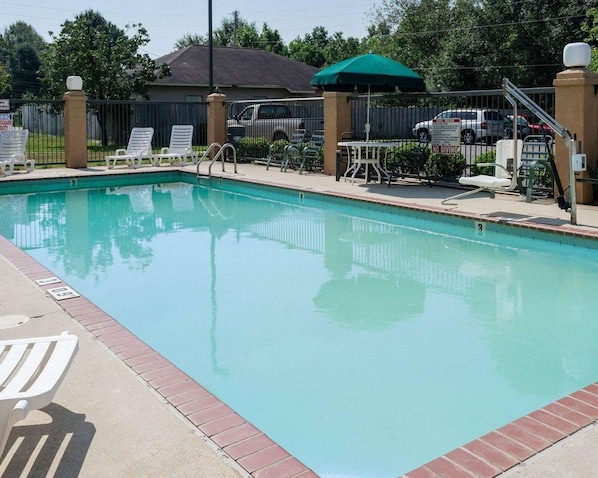A rectangular swimming pool with a tiled edge, surrounded by a brick walkway. There are white lounge chairs and a green umbrella on the poolside. - Quality Inn Magee,ms (Magee)