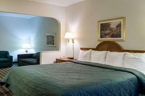 A hotel room with a large bed, a nightstand, a lamp, a chair, and a painting on the wall.