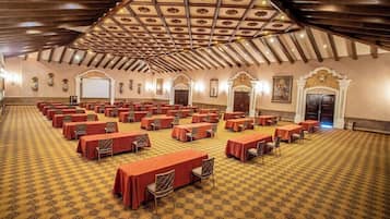 A large hall with rows of tables and chairs, a patterned carpet, and a high ceiling with wooden beams.