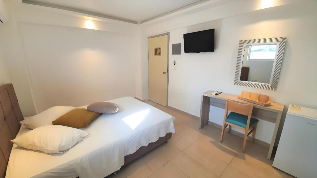 Un dormitorio con cama, escritorio, silla, televisión y espejo.