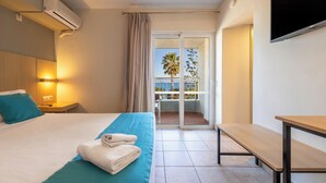 Habitación de hotel con cama, una banca, televisión y balcón con vistas.