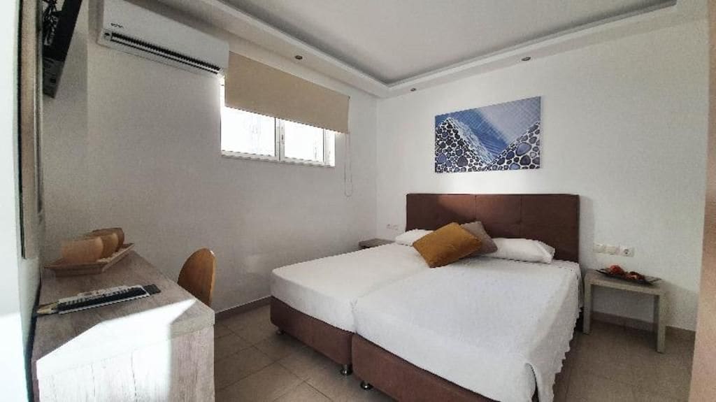 Habitación de hotel con cama, escritorio, silla, ventana y una obra de arte colgada en la pared.