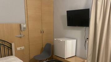A bedroom with a bed, a wardrobe, a desk with a computer, a TV, and a curtain.