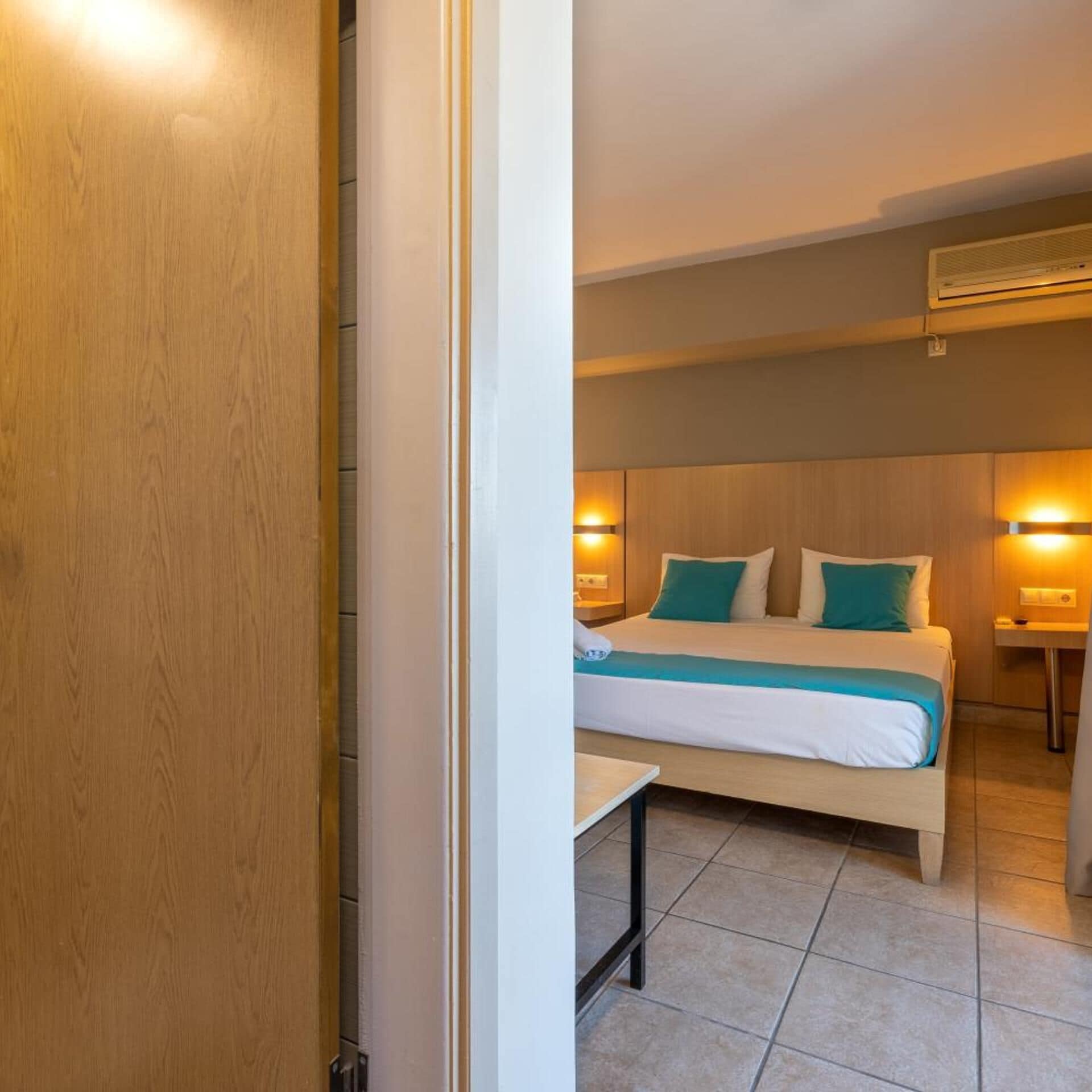 Una habitación de hotel con una cama, mesitas de noche y un aire acondicionado de pared.