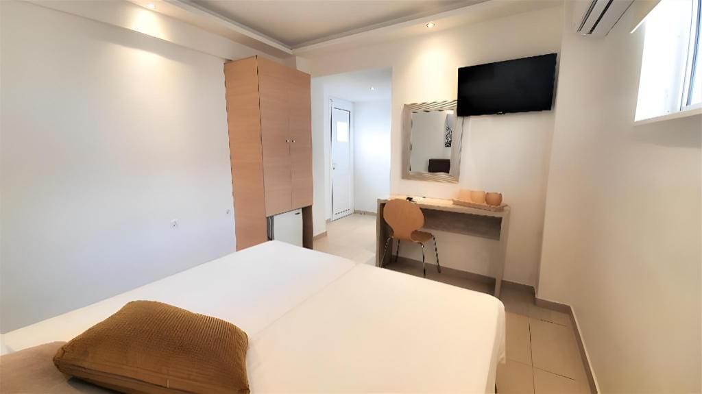 A bedroom with a bed, a desk, a chair, a wardrobe, a TV, and a window.