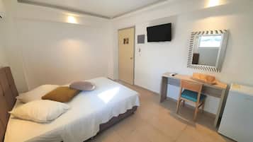 Un dormitorio con cama, escritorio, silla, televisión y espejo.