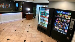 Un vestíbulo de hotel con una recepción, una máquina expendedora de aperitivos y bebidas, y un piso de baldosas.
