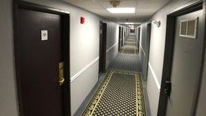 Pasillo de hotel con puertas numeradas 121 y 122, alfombra estampada y techo con detector de humo.