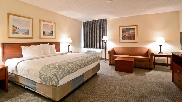 Habitación de hotel con cama, sofá, sillón, escritorio y dos cuadros en la pared.