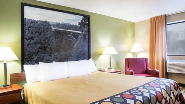 A hotel room with a bed, two bedside lamps, a red armchair, a large framed picture on the wall, and a window with curtains. - Spark by Hilton Beckley (Beckley)