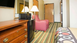 A hotel room with a wooden dresser, a black refrigerator, a pink chair, a bed with a striped bedspread, a television, and a mirror. - Spark by Hilton Beckley (Beckley)