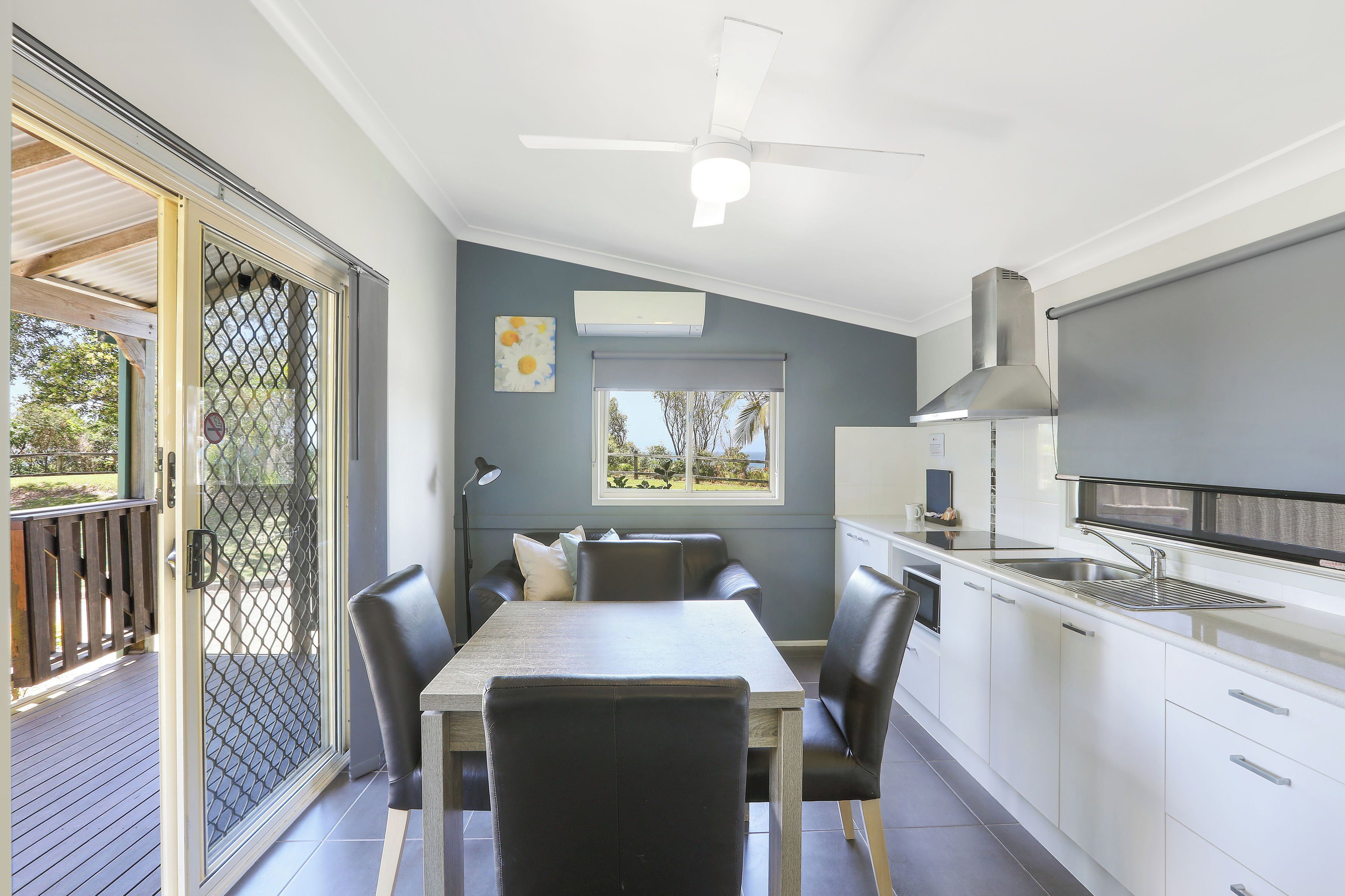 A modern kitchen with a dining area, a ceiling fan, and a view through the window.