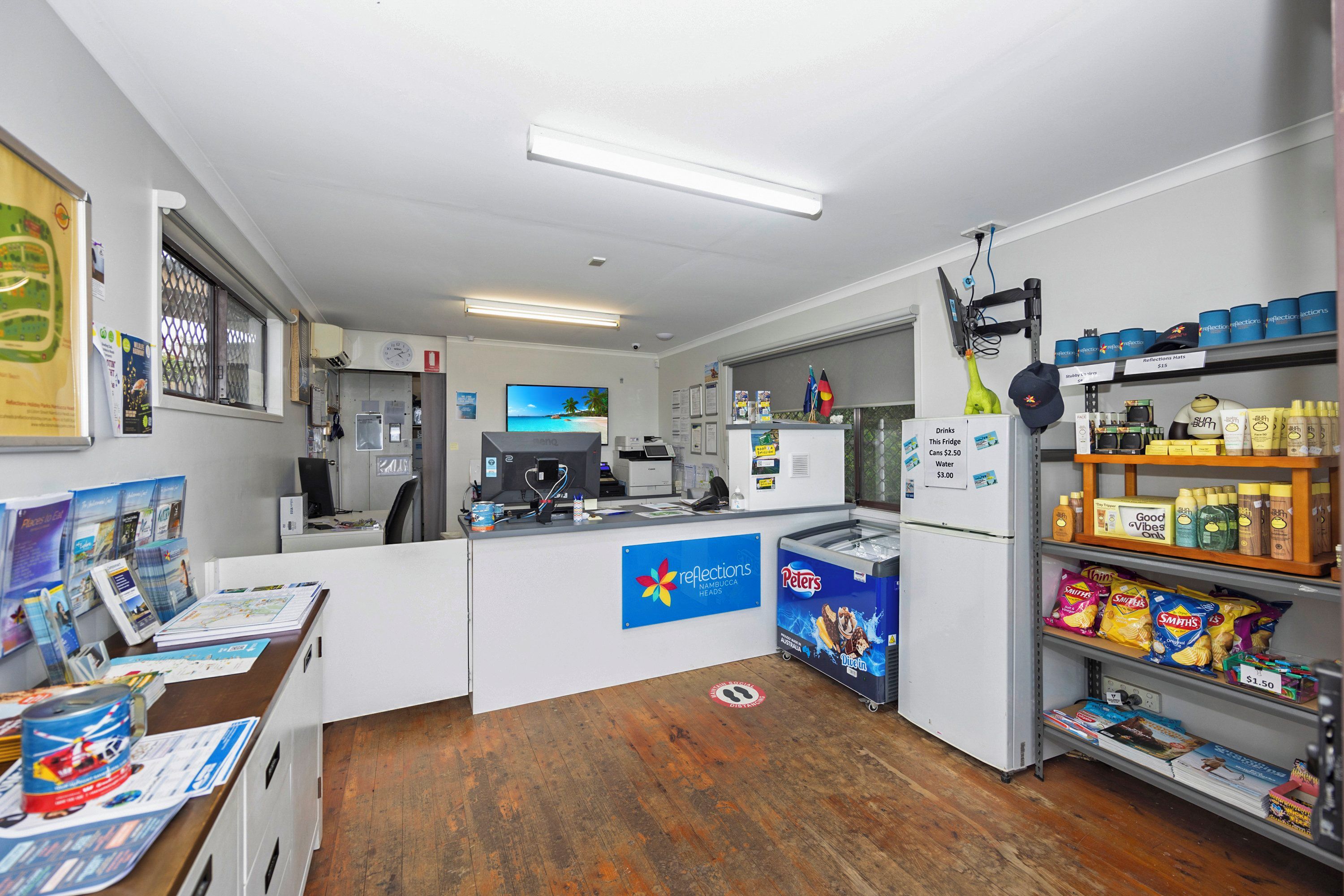A small, well-lit room with a counter, a refrigerator stocked with snacks, and a display of travel brochures.