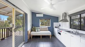 A compact living space with a balcony, a bed, a kitchenette, and a ceiling fan.