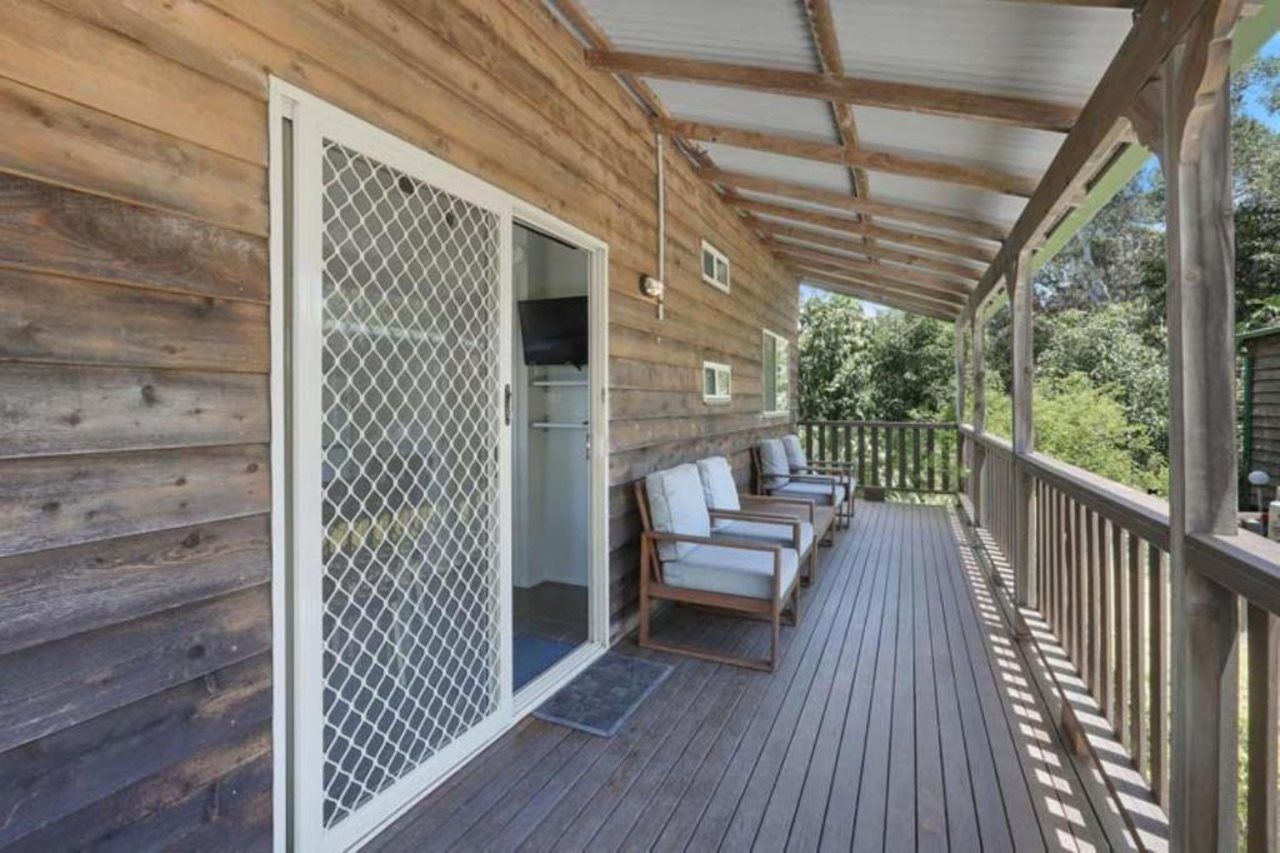 A wooden deck with a covered area, sliding glass doors, and a row of chairs.