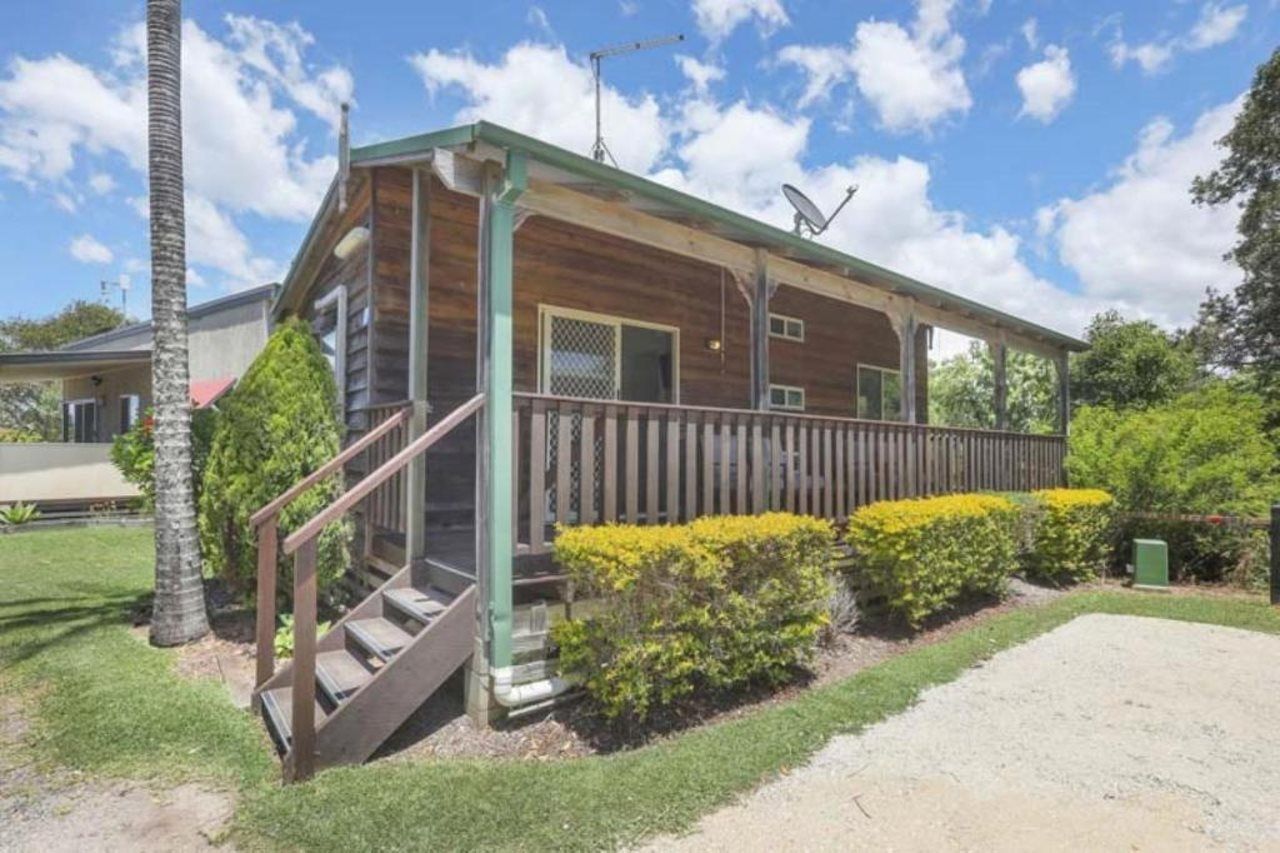 A two-story wooden cabin with a porch, a staircase, and a satellite dish.