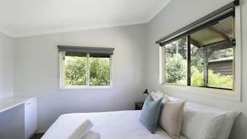A bedroom with a bed, a desk, and two windows.