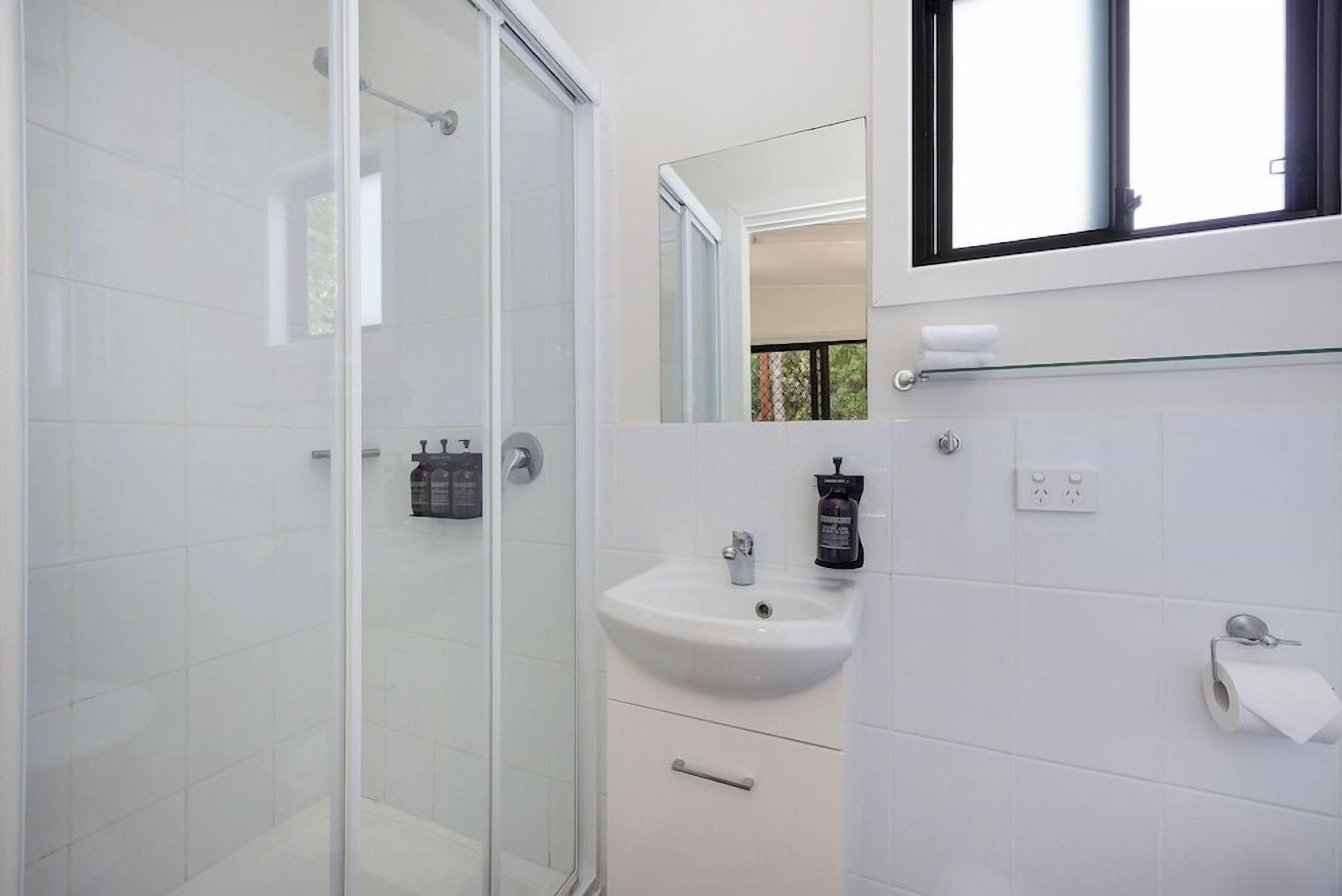 Een moderne badkamer met een douchecabine van glas, een witte wastafel met spiegel erboven en een klein raam voor natuurlijk licht.