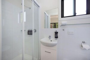 Un baño moderno con cabina de ducha de vidrio, un lavamanos blanco con un espejo encima y un ventanal que proporciona luz natural.