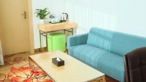 A room with a blue sofa, a small table with a tissue box, a green trash bin, and a wooden desk with a plant and a kettle. - Greentree Inn Linxia Autonomous Prefecture Linxia Oxford River Avenue Express Hotel (Linxia)