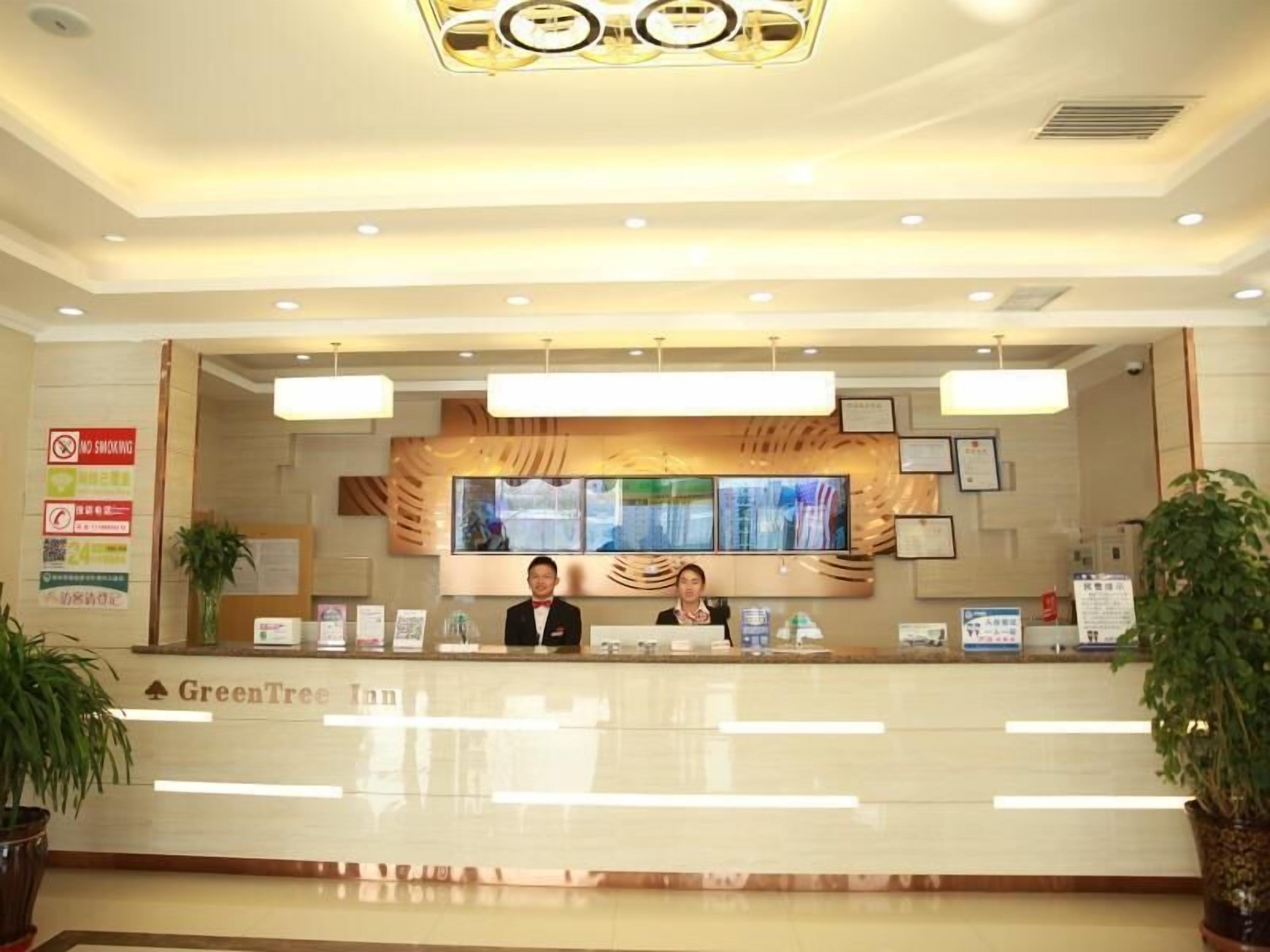 A hotel reception desk with a modern design, a large screen, and a sign for GreenTree Inn.