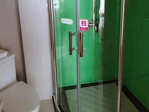 Une salle de bain avec des toilettes, une douche à parois de verre et un mur vert.