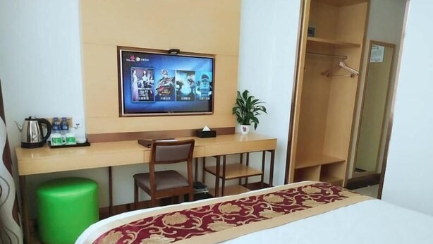 A hotel room with a bed, a desk with a chair, a television, a green trash bin, and a potted plant. - Greentree Inn Linxia Autonomous Prefecture Linxia Oxford River Avenue Express Hotel (Linxia)