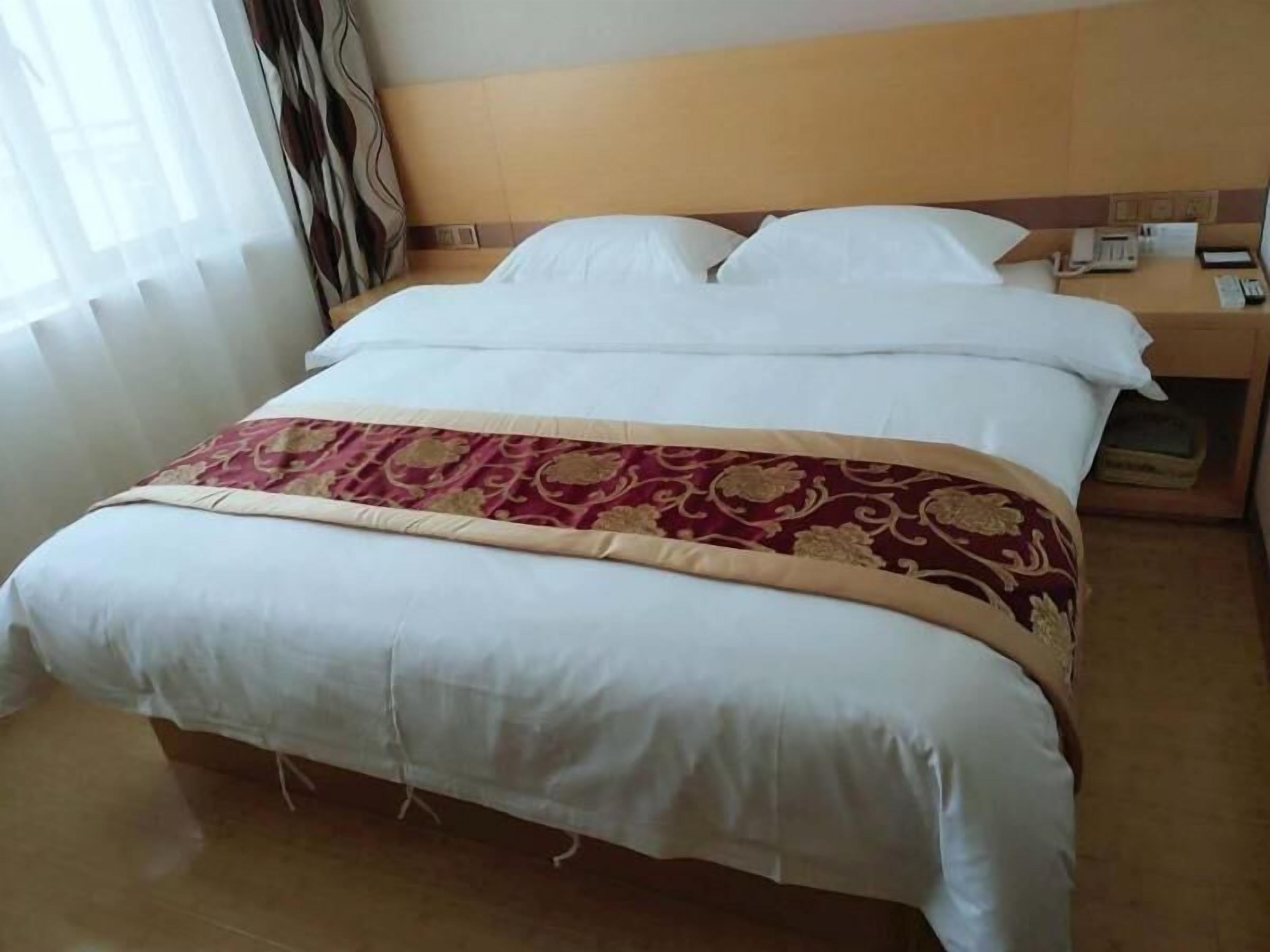 A hotel room with a bed, a bedside table with a phone, and a window with curtains.