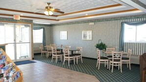 A lobby with striped wallpaper, a ceiling fan, a reception desk, and a dining area with chairs and tables.