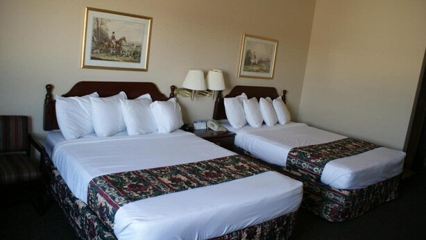 A hotel room with two single beds, a nightstand with a lamp, a chair, and two framed pictures on the wall.