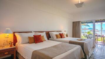 Quarto de hotel com duas camas, uma mesa de cabeceira, uma mesa com abajur e vista para o oceano através de uma porta de correr.