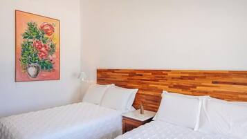 Quarto de hotel com duas camas, uma cabeceira de madeira, um quadro de flores e uma mesa de cabeceira com abajur.