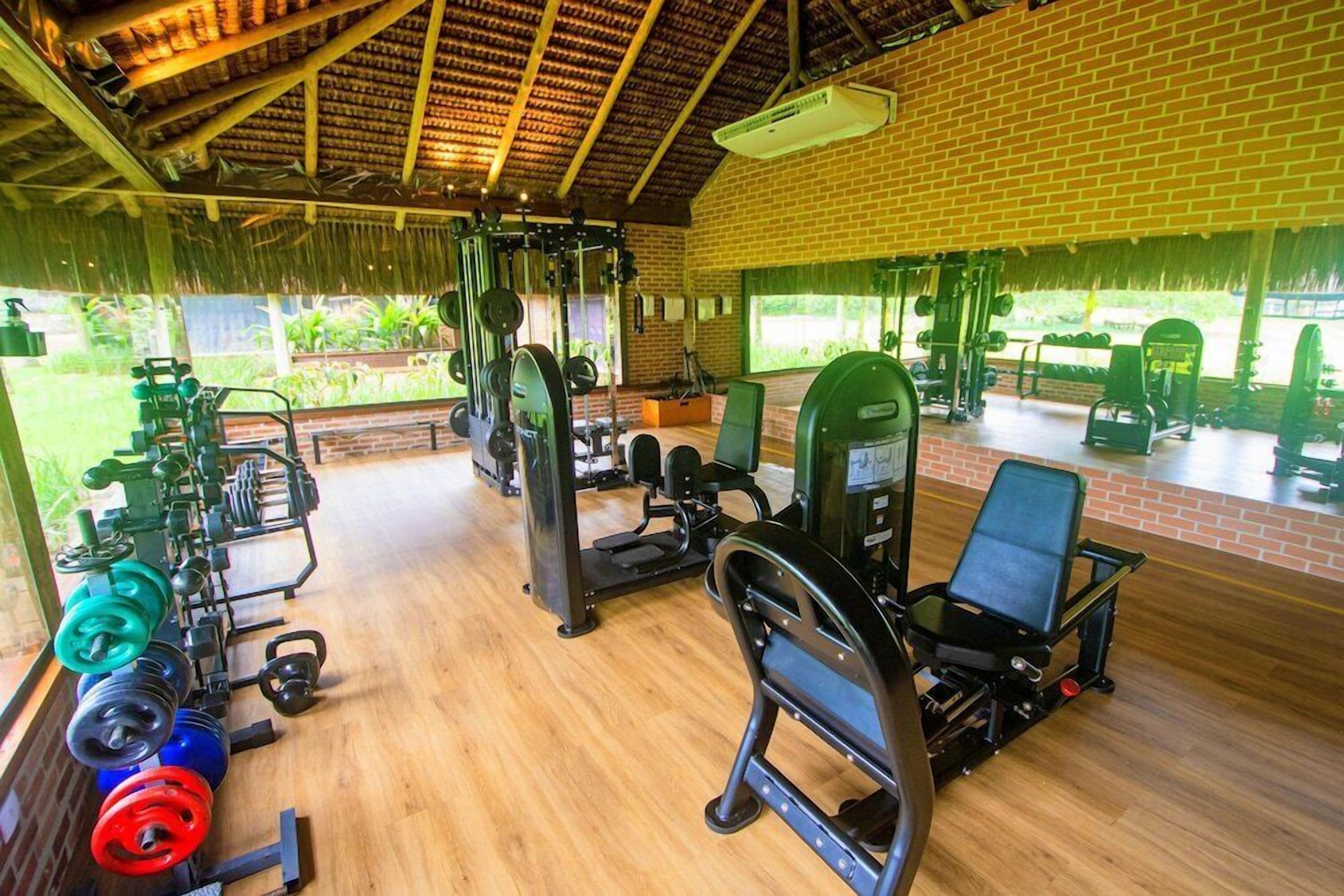 Uma academia com diversos equipamentos de exercício, parede de tijolos e janelas amplas.