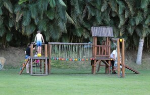 A wooden play structure with a rope bridge and climbing net, surrounded by palm trees. - Portobello Hotel Resort AND Safari (Mangaratiba)