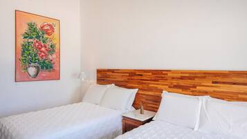 Une chambre d’hôtel avec deux lits, une tête de lit en bois, un tableau représentant des fleurs et une table de chevet avec une lampe.
