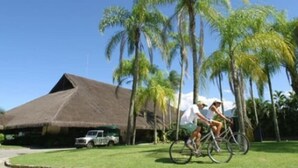 A thatched-roof building with a lawn and palm trees. - Portobello Hotel Resort And Safari (Mangaratiba)