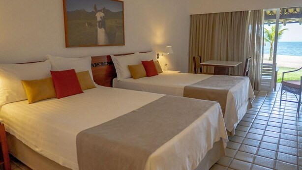 A hotel room with two beds, a painting, a table, and a view of the beach. - Portobello Hotel Resort And Safari (Mangaratiba)