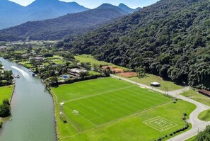 Um rio serpenteando por um vale, com um campo de futebol e edifícios na margem oposta.