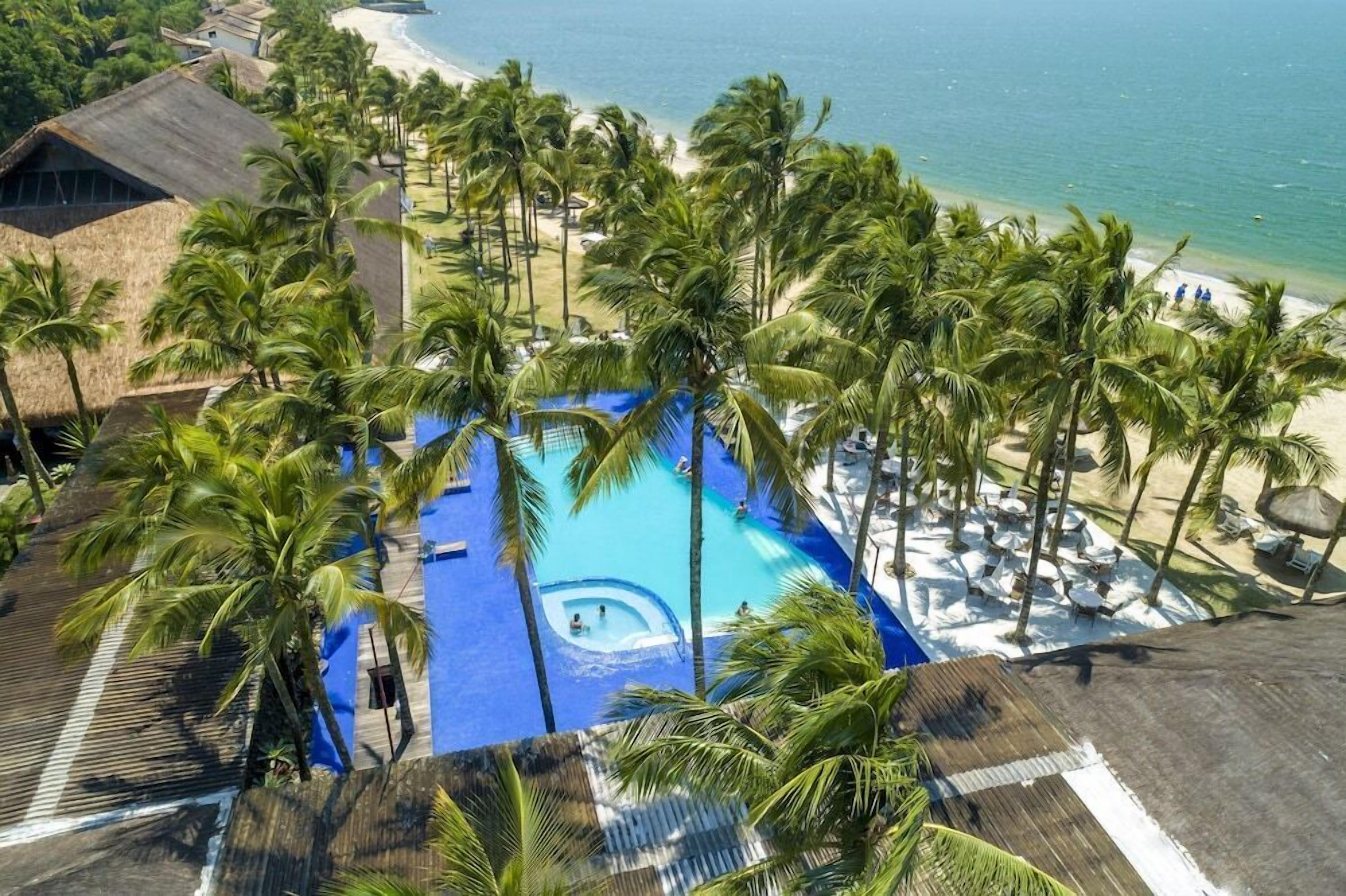 Um resort com piscina, rodeado por palmeiras, uma praia e vista para o oceano.